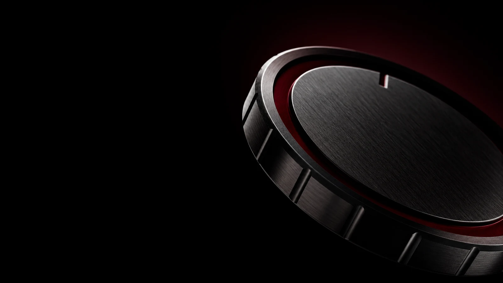A machined graphite medallion with a deep oxblood-anodised bevel, catching a hard rim light against black.